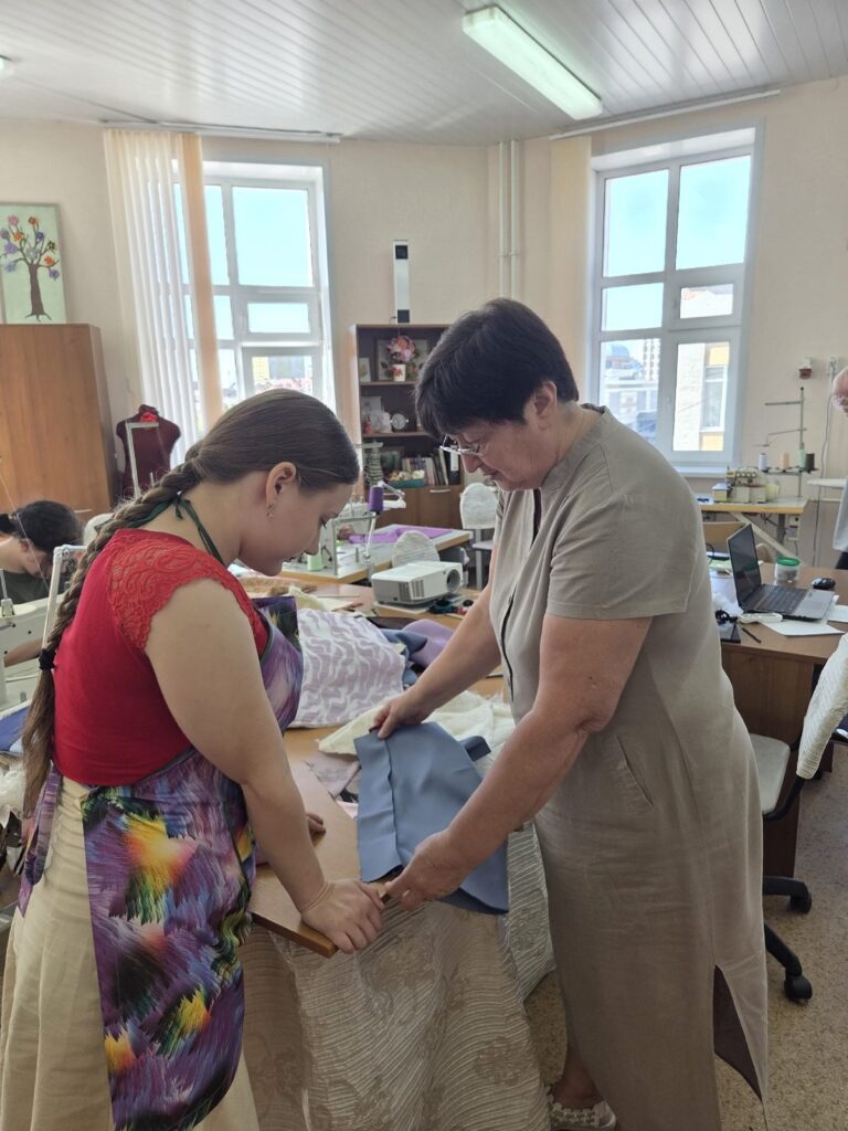 Мастер производственного обучения показывает обучающейся приёмы работы с тканью в швейной мастерской
